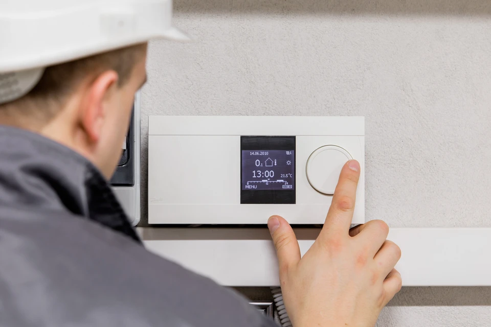 Technicien en casquette ajustant un thermostat programmable mural dans un intérieur résidentiel
