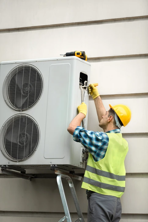 Technicien en équipement de protection individuelle installant une unité de climatisation extérieure sur façade résidentielle