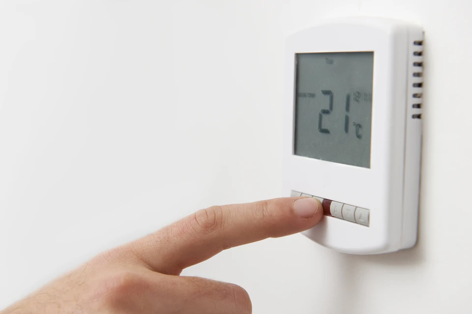 Une main ajuste un thermostat numérique mural blanc affichant 21°C