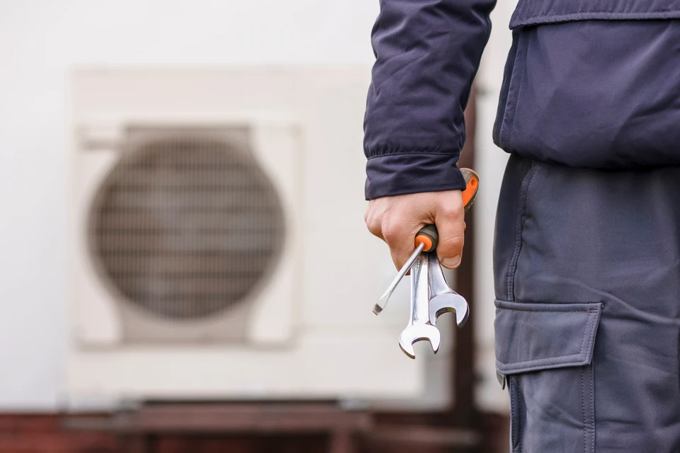 Main dans un intérieur blanc tenant une télécommande de climatiseur affichant 25°C
