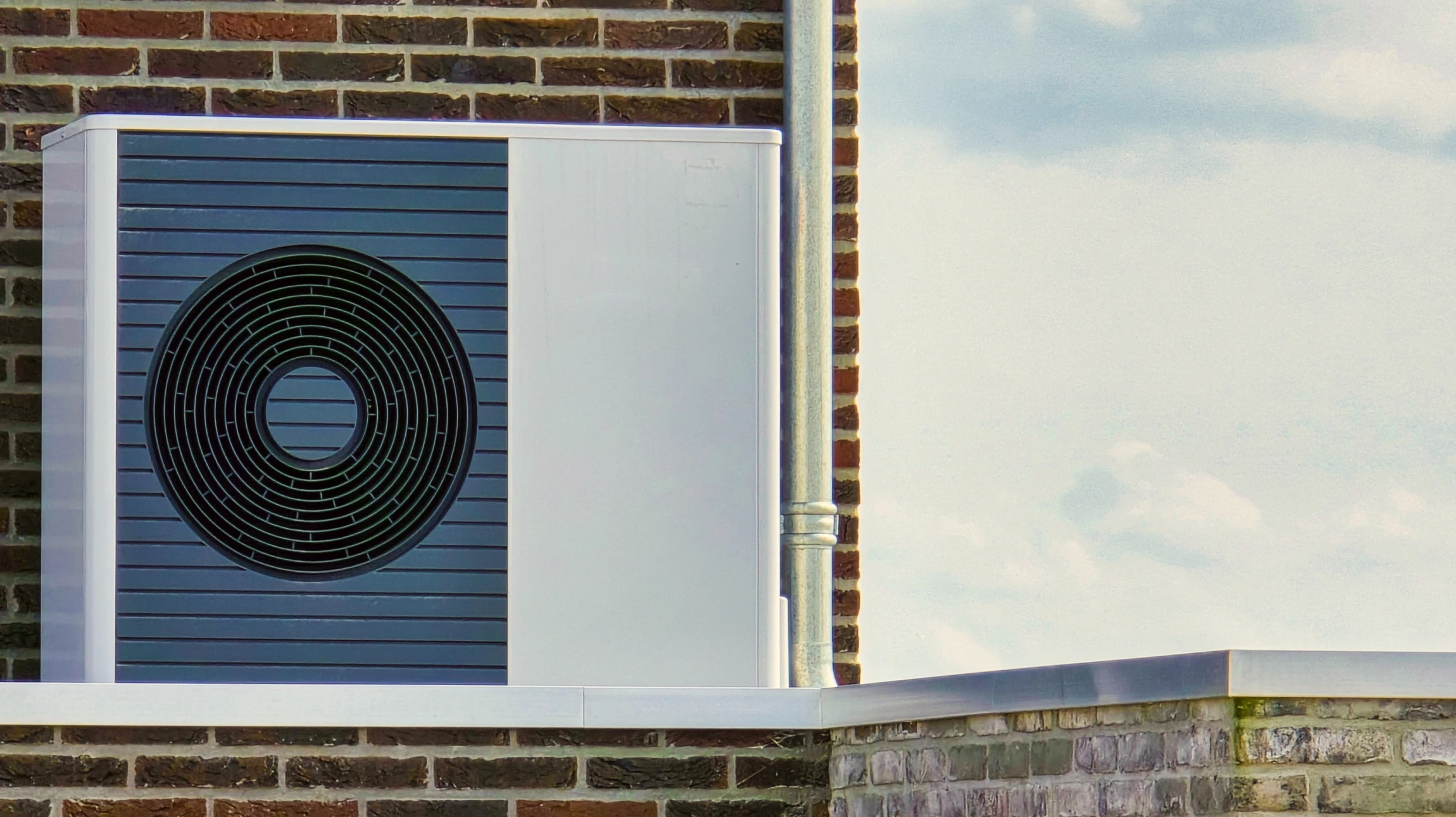 Extérieur résidentiel moderne avec pompe à chaleur air-eau installée sur dalle béton près d'un mur blanc