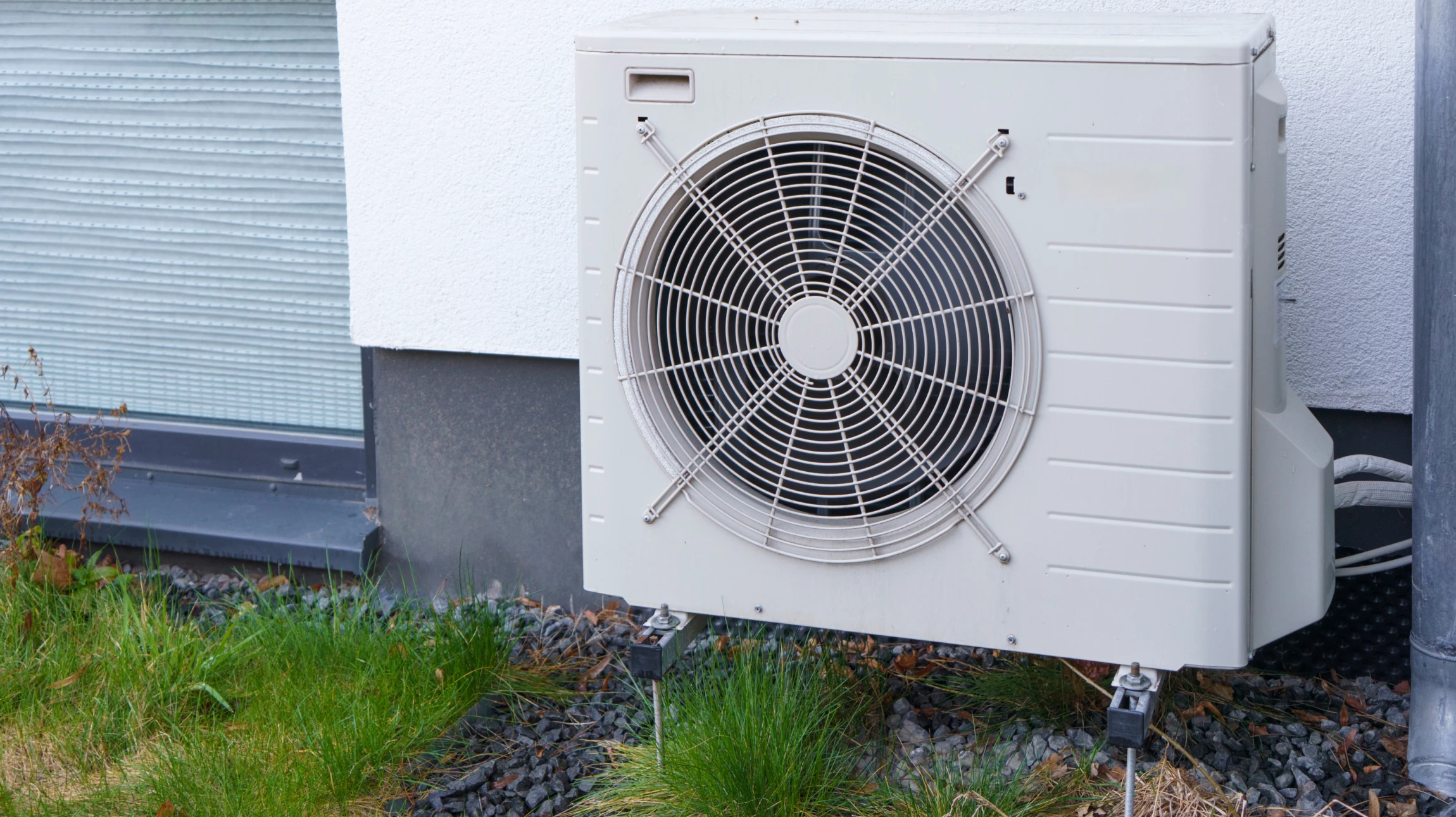 Technicien en équipement de protection individuelle installant une unité de climatisation extérieure sur façade résidentielle