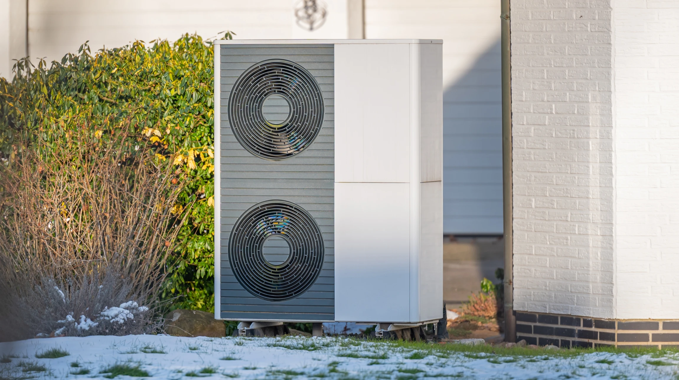 Extérieur résidentiel avec pompe à chaleur air-eau installée sur terrasse pavée contre mur de briques