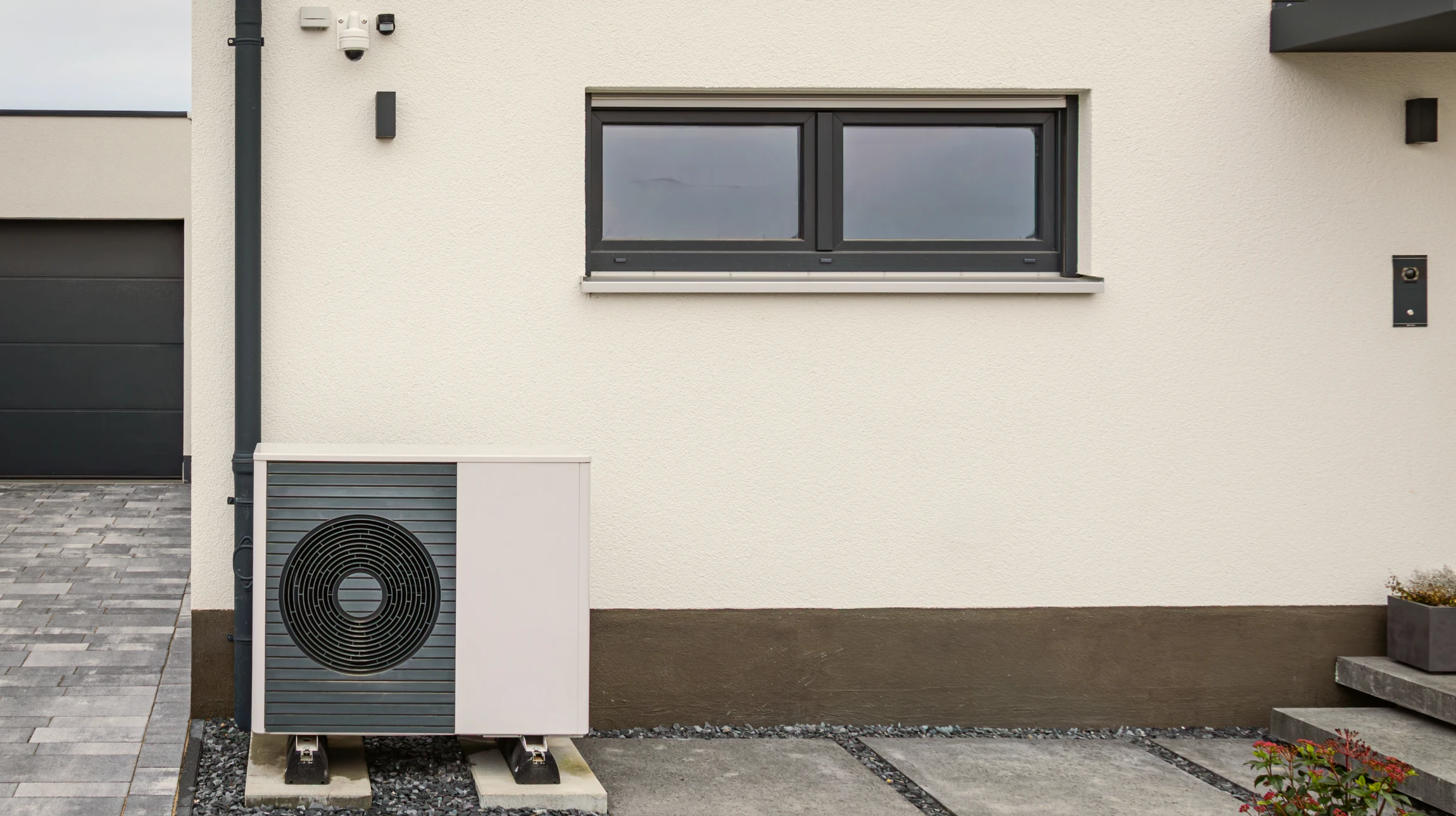 Extérieur résidentiel avec pompe à chaleur air-eau installée sur terrasse pavée contre mur de briques